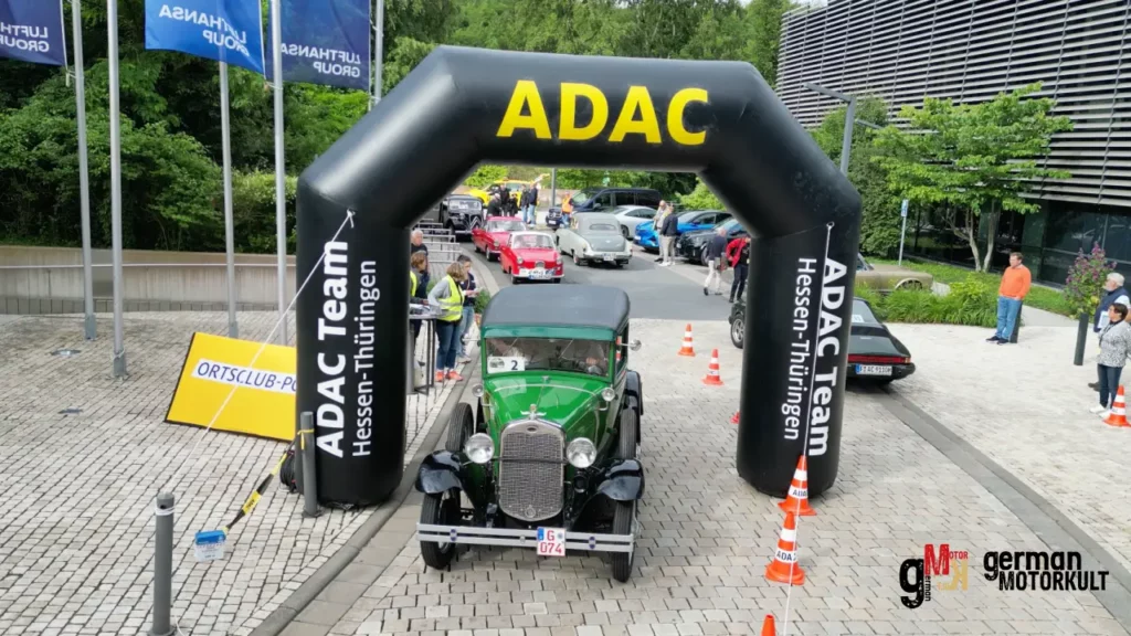 Grüner Oldtimer-Wagen fährt unter ADAC-Zielportal bei der Oldtimerfahrt durch Hessen, im Hintergrund weitere Teilnehmer und Zuschauer